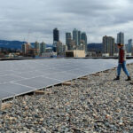 Two people stand in front of a solar array on the roof of a building.