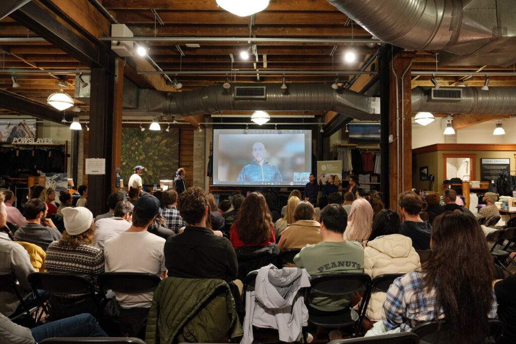 Wide shot from behind of an audience looking at a projector screen.