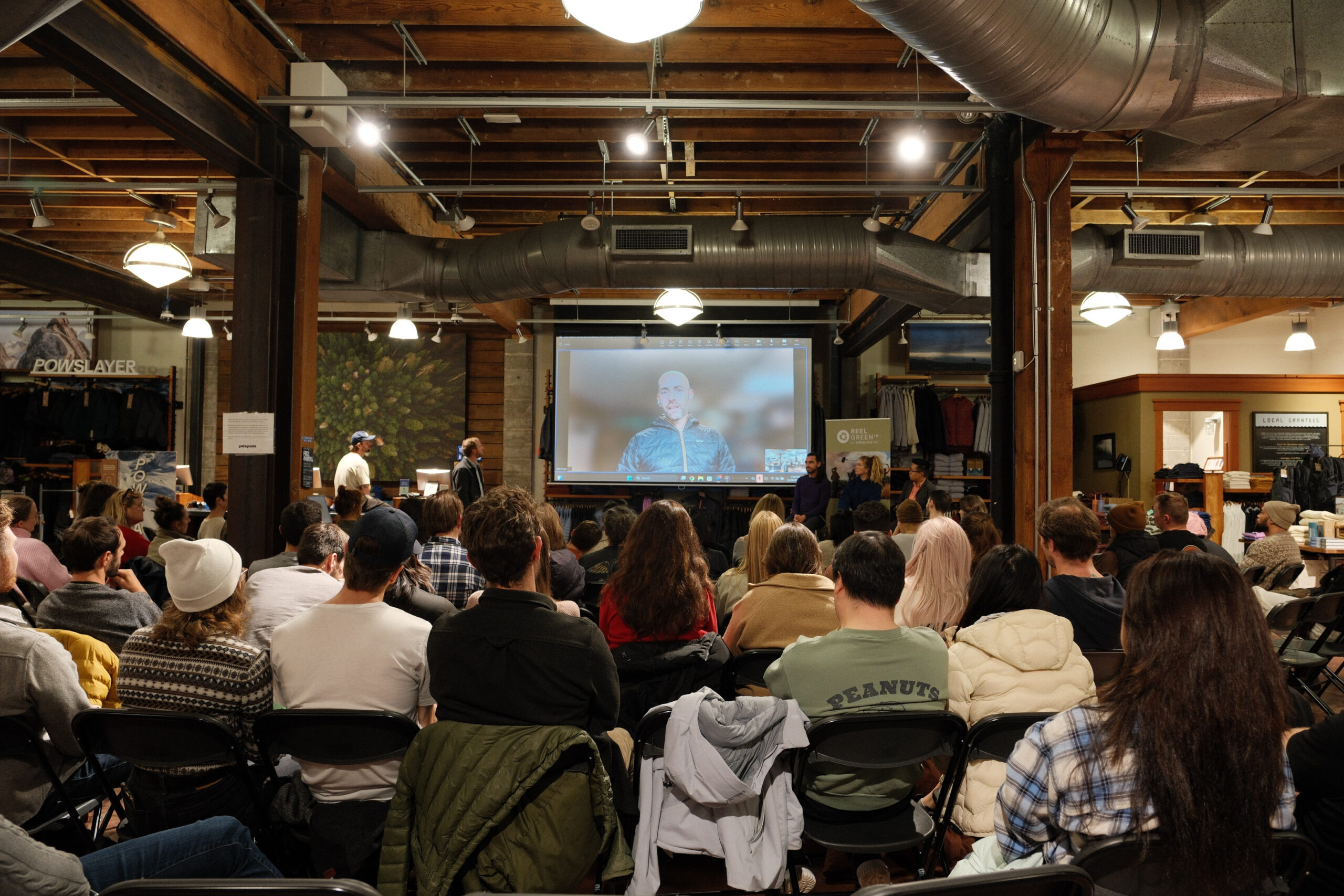 Wide shot from behind of an audience looking at a projector screen.